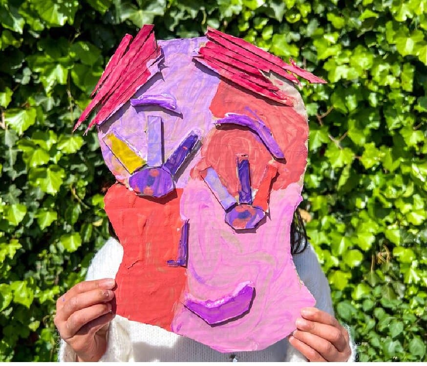 The Cardboard Days cover photo, a kid holding a giant painted cardboard face